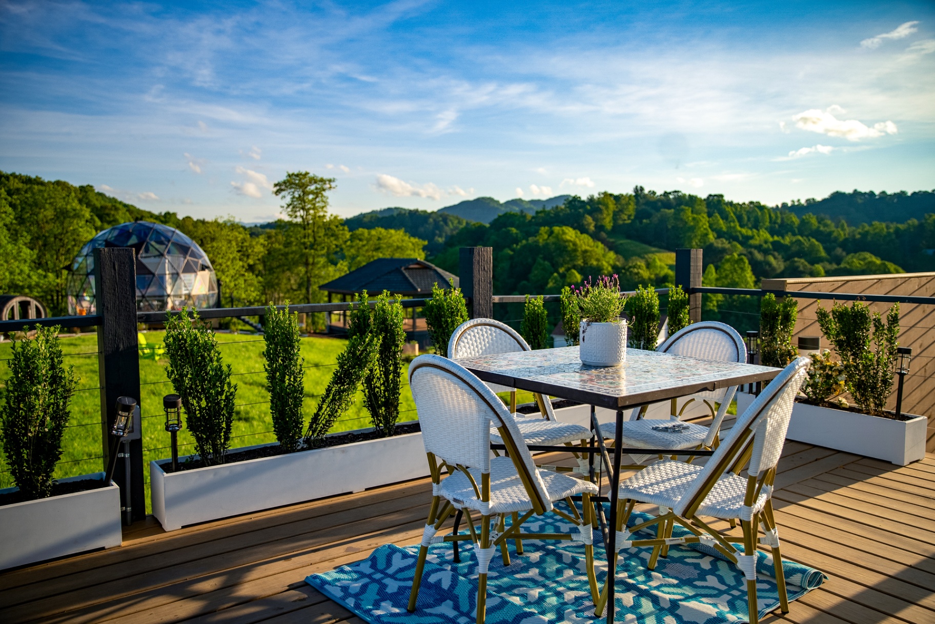 Mosaic bistro table and white rattan chairs on a private deck overlooking the meadow and glass dome