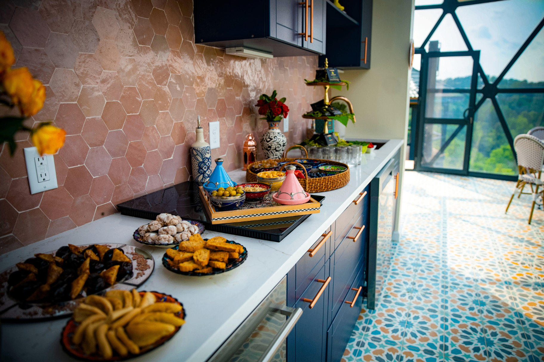 Moroccan kitchen with terracotta hex tile, patterned floor, and a spread of tagines, olives, pastries and mint tea
