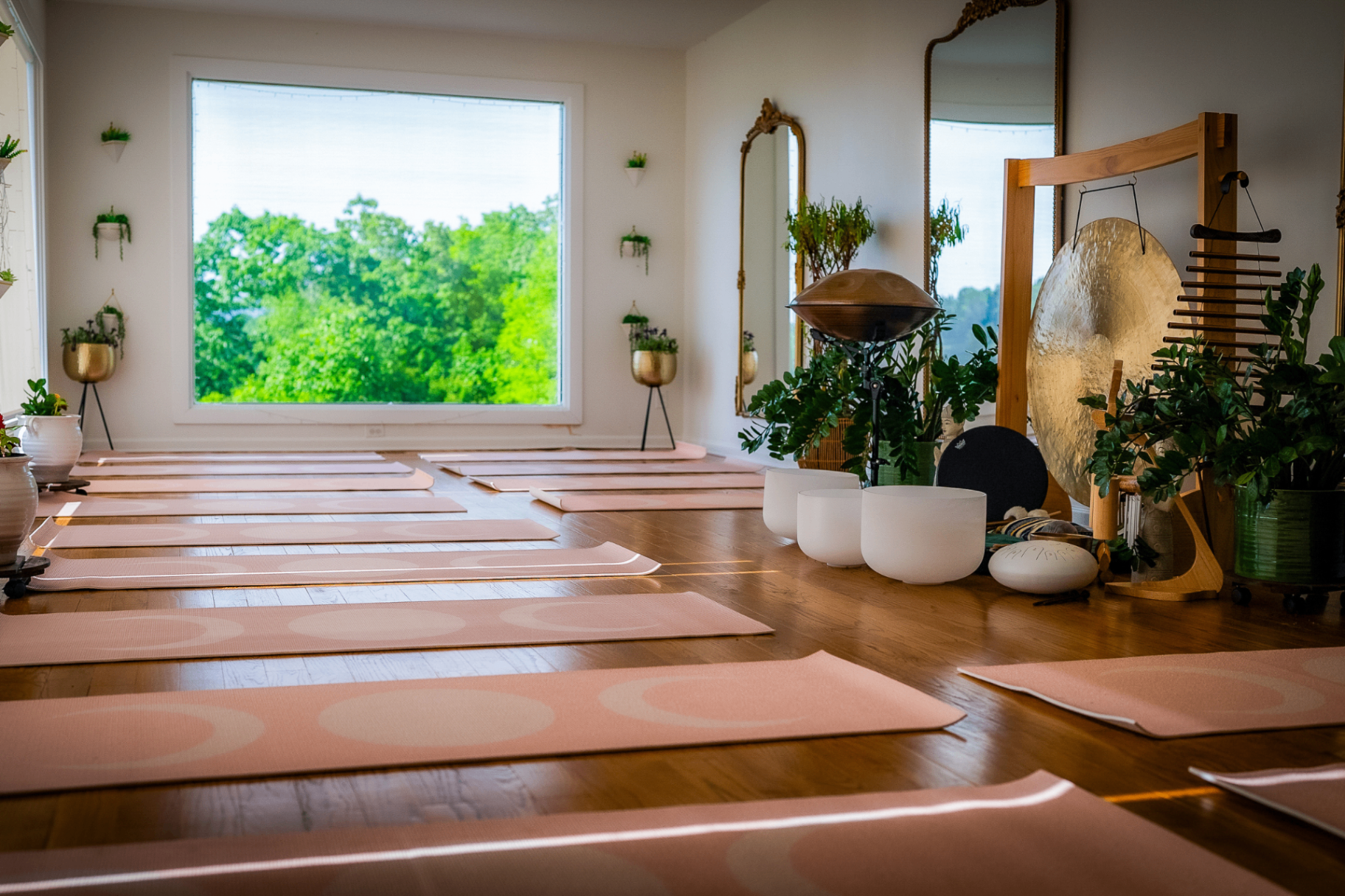 Yoga studio with pink mats laid out, gong and crystal singing bowls, a large window framing the trees