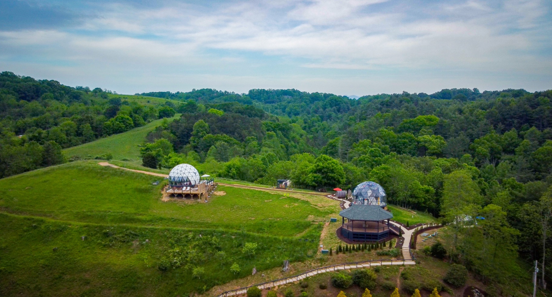 Aerial view of two geodesic domes and the pavilion set across the meadow with forest behind