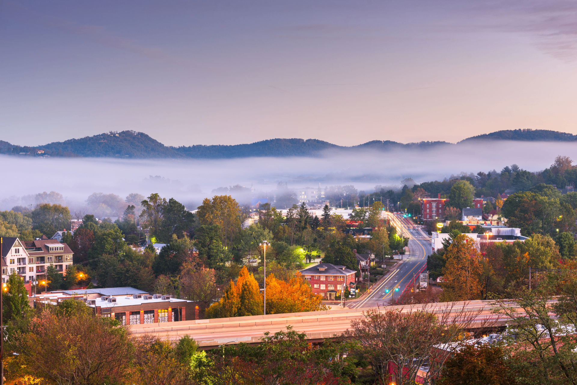 Downtown Asheville skyline at dusk with mountains and valley fog