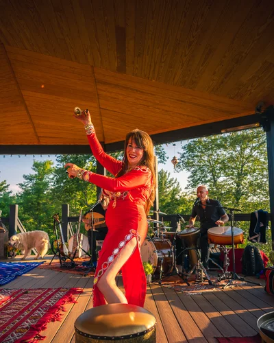 Belly dancer in a red gown performing with the live band under the pavilion at golden hour