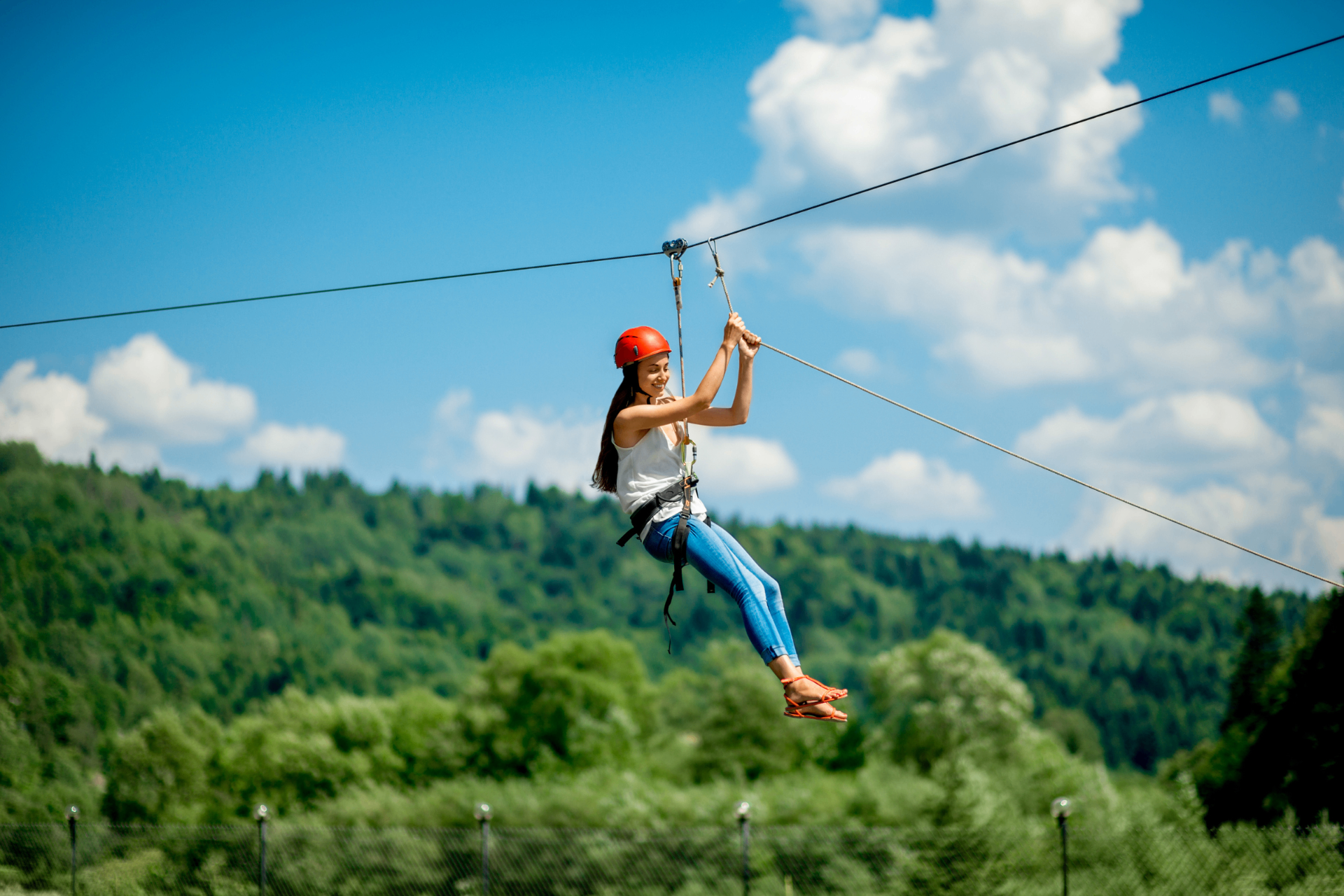 A woman ziplining above the forest canopy with mountain views and blue sky