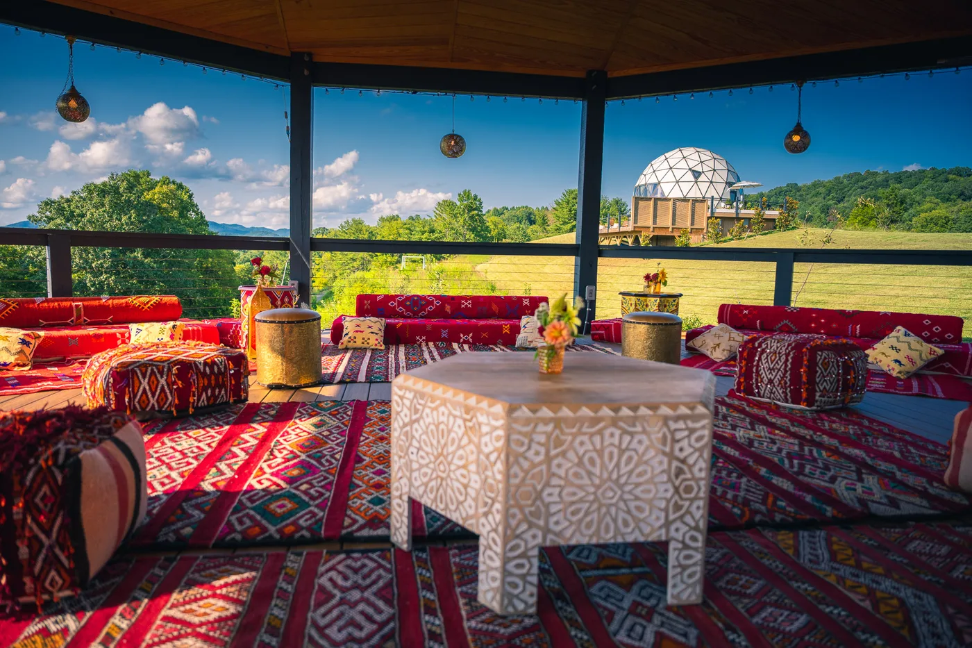Moroccan floor seating, kilims and lanterns in the Medina pavilion at Munaya, with the geodesic dome and Blue Ridge mountains beyond.