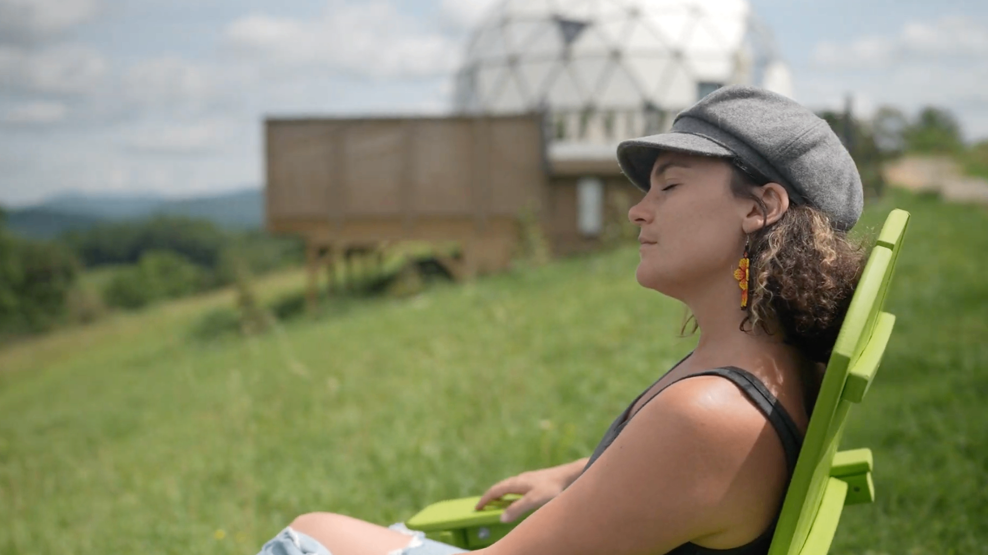 A guest reclines in a chair on the meadow with a Moroccan dome and mountains behind her.