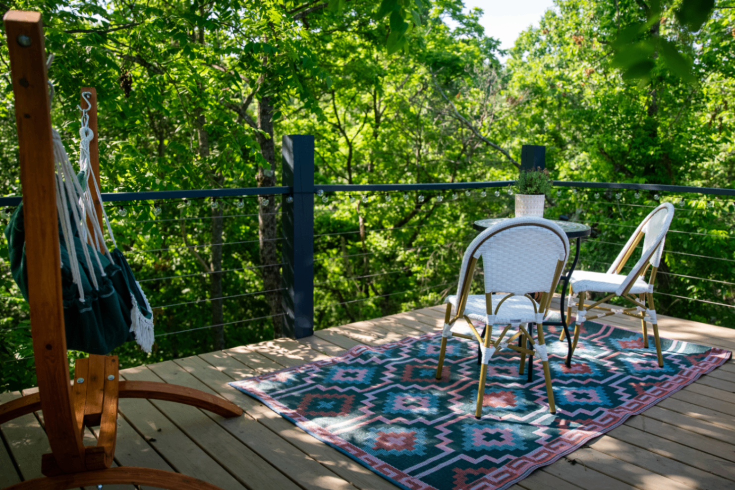 Shaded deck with a green hammock chair, bistro chairs, and kilim rug under string lights