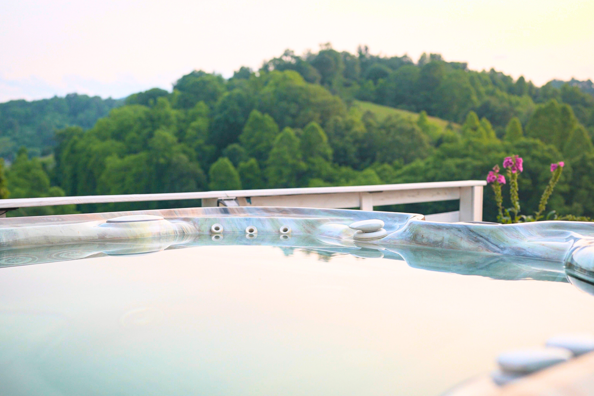 Surface of the hot tub with still steaming water, pearl-marbled rim, and the green Blue Ridge hills soft-focused beyond