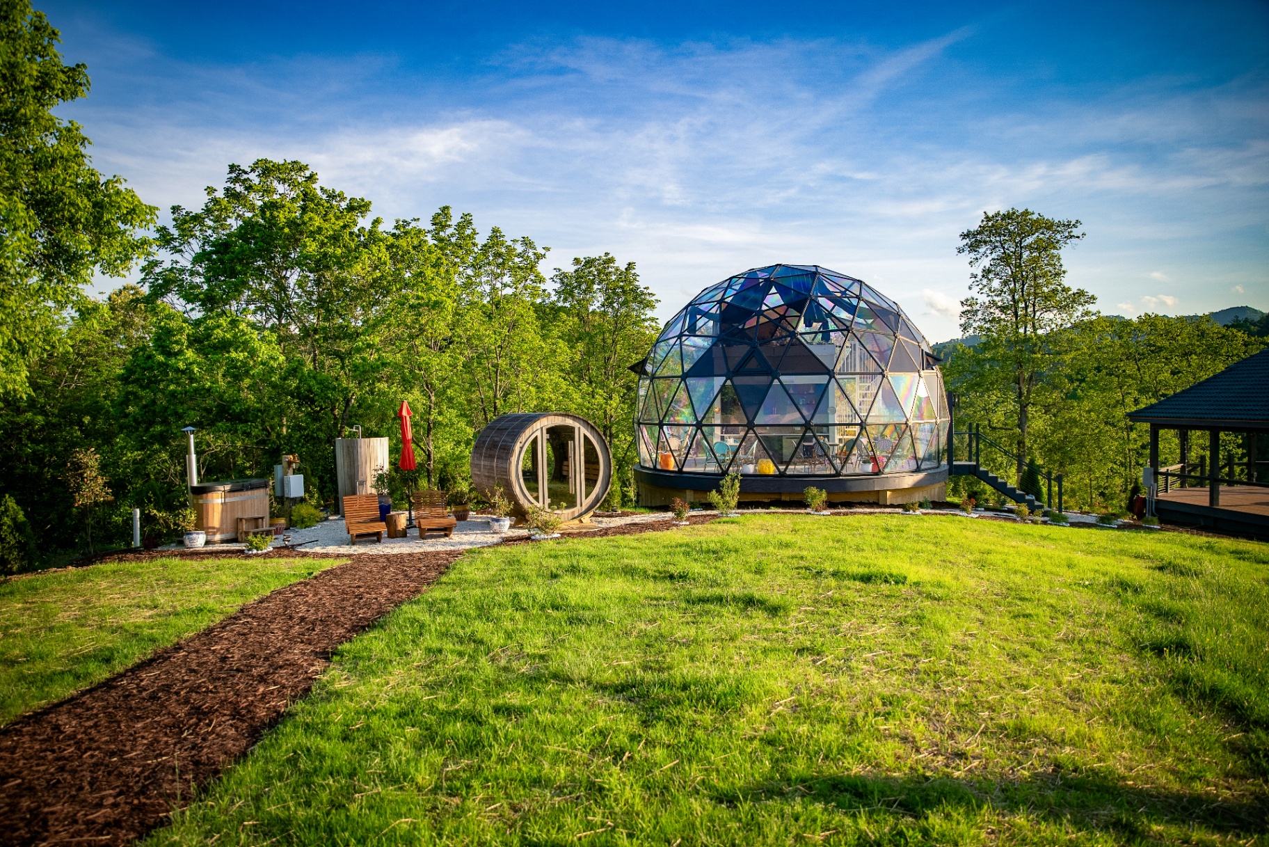 Iridescent glass dome with cedar barrel sauna and hot tub set on the meadow with trees behind