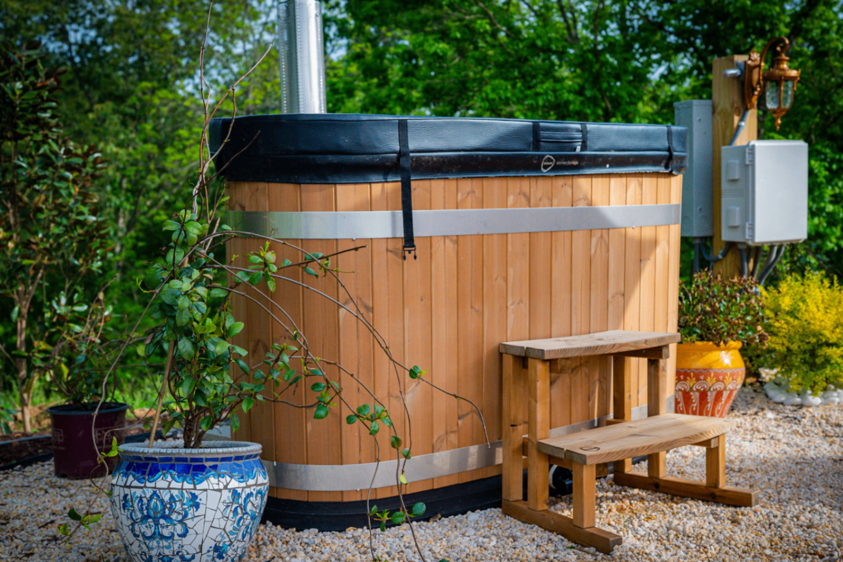 Wood-fired cedar hot tub with chimney flanked by hand-painted blue-and-white Moroccan mosaic planters and a terracotta urn