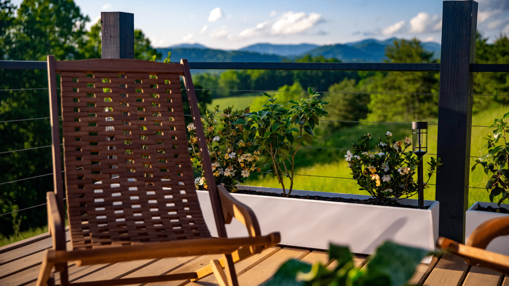Woven wooden lounge chair on a private deck with flowering planters looking out to the Blue Ridge Mountains