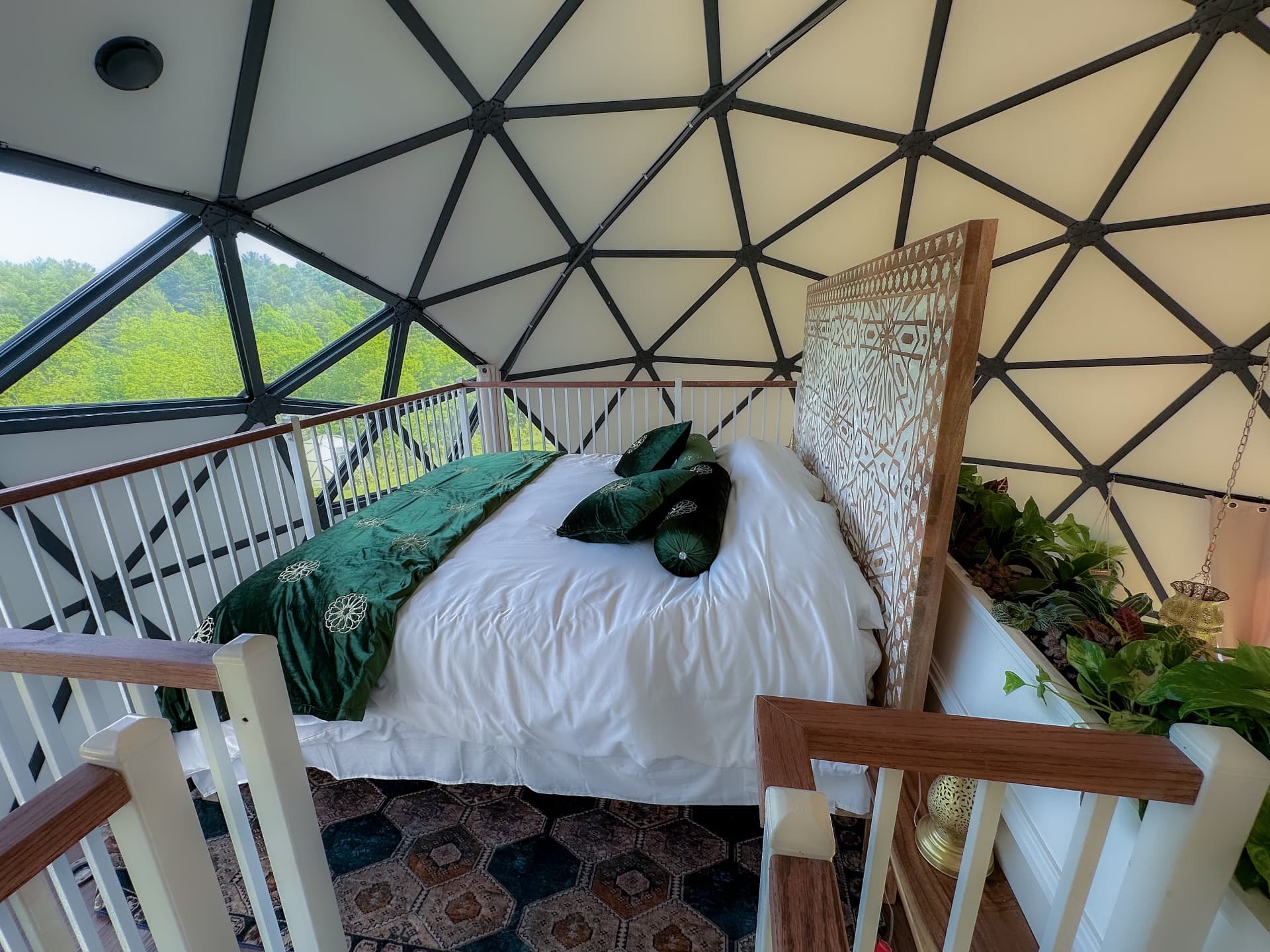 The loft bed inside Casablanca Dome beneath the geodesic panels, looking out to the green hills