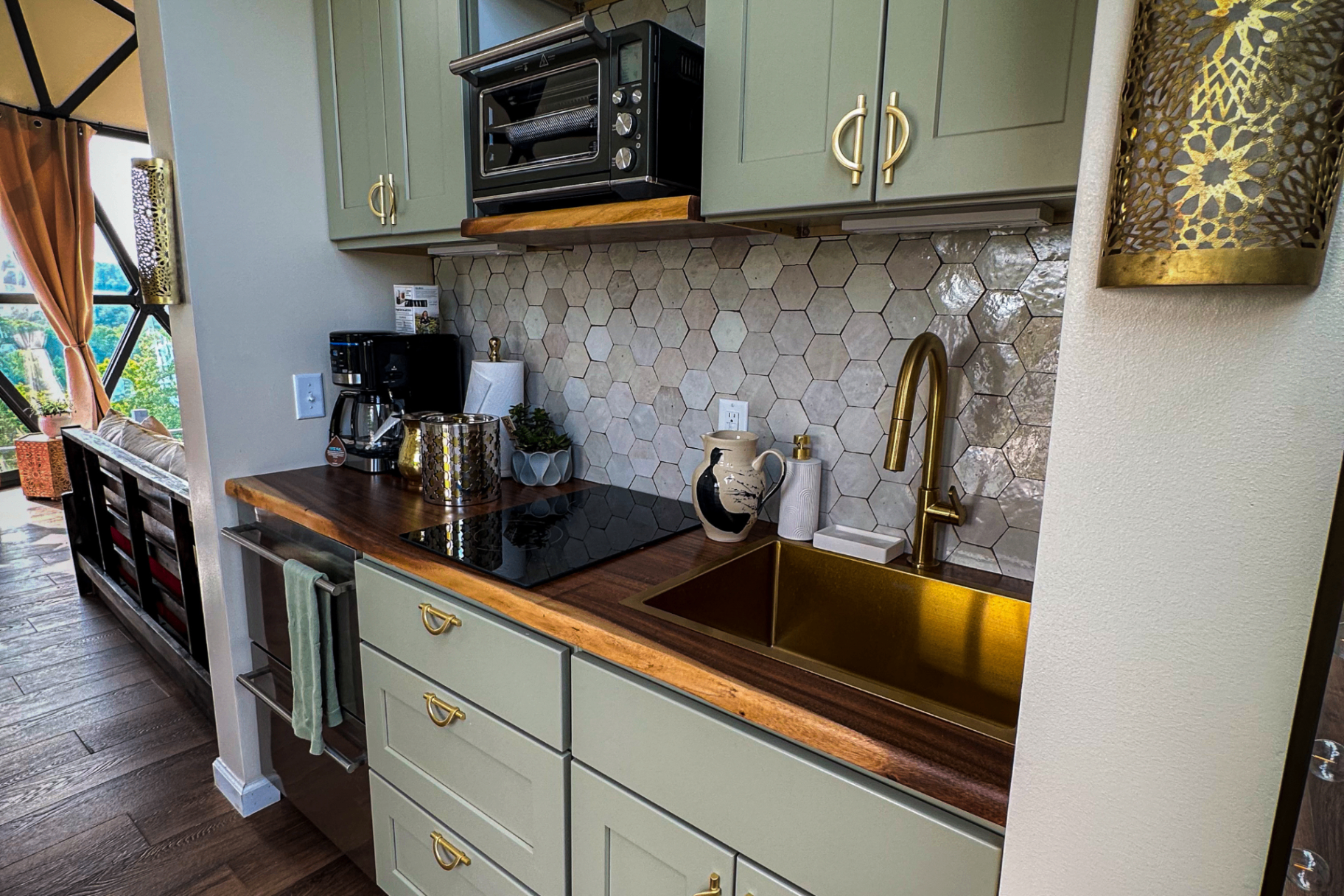 Medina Tea House kitchen with sage cabinetry, gold sink, hexagonal tile, and pierced brass sconce