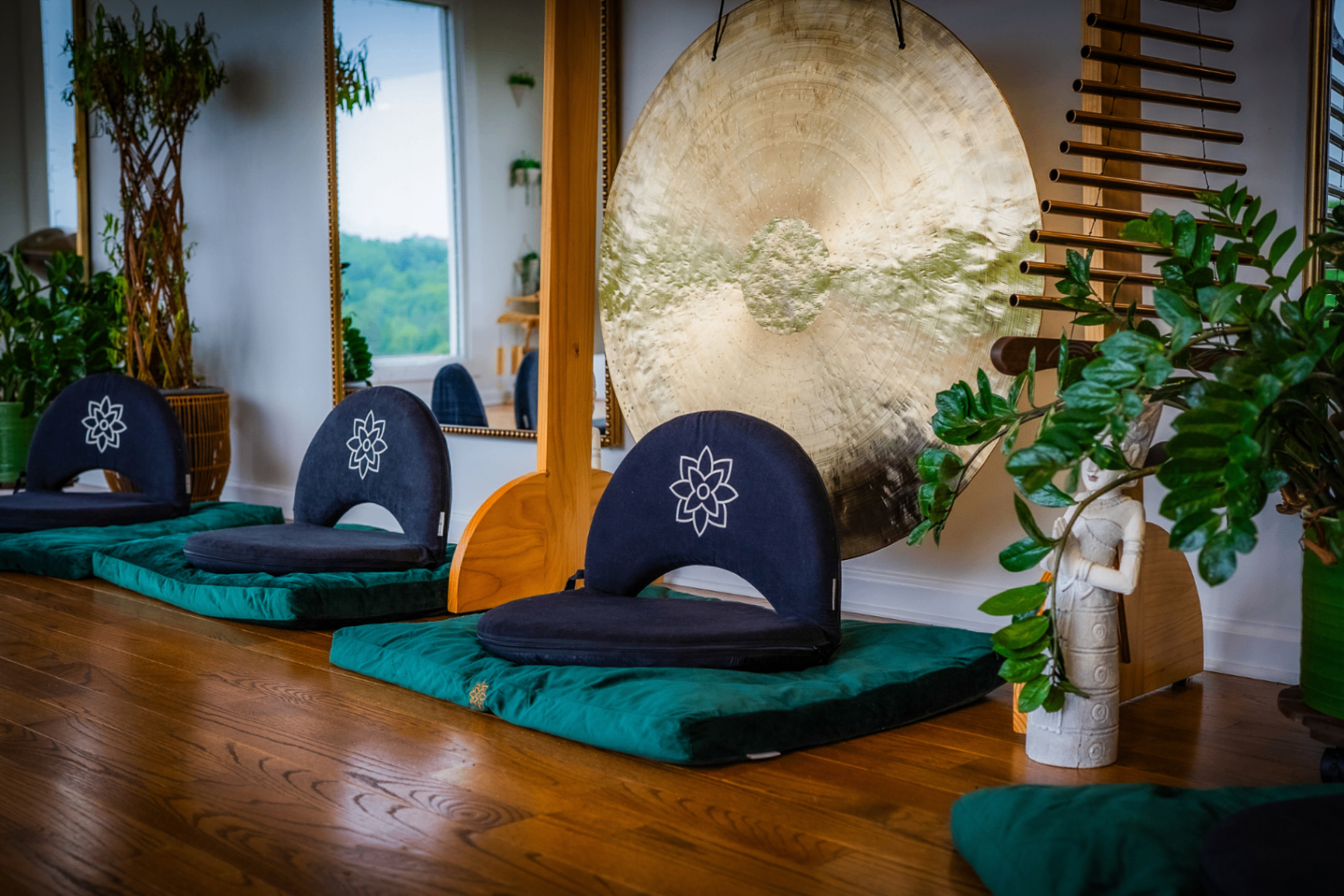 Meditation seats on green cushions in front of a large brass gong and gilded mirror
