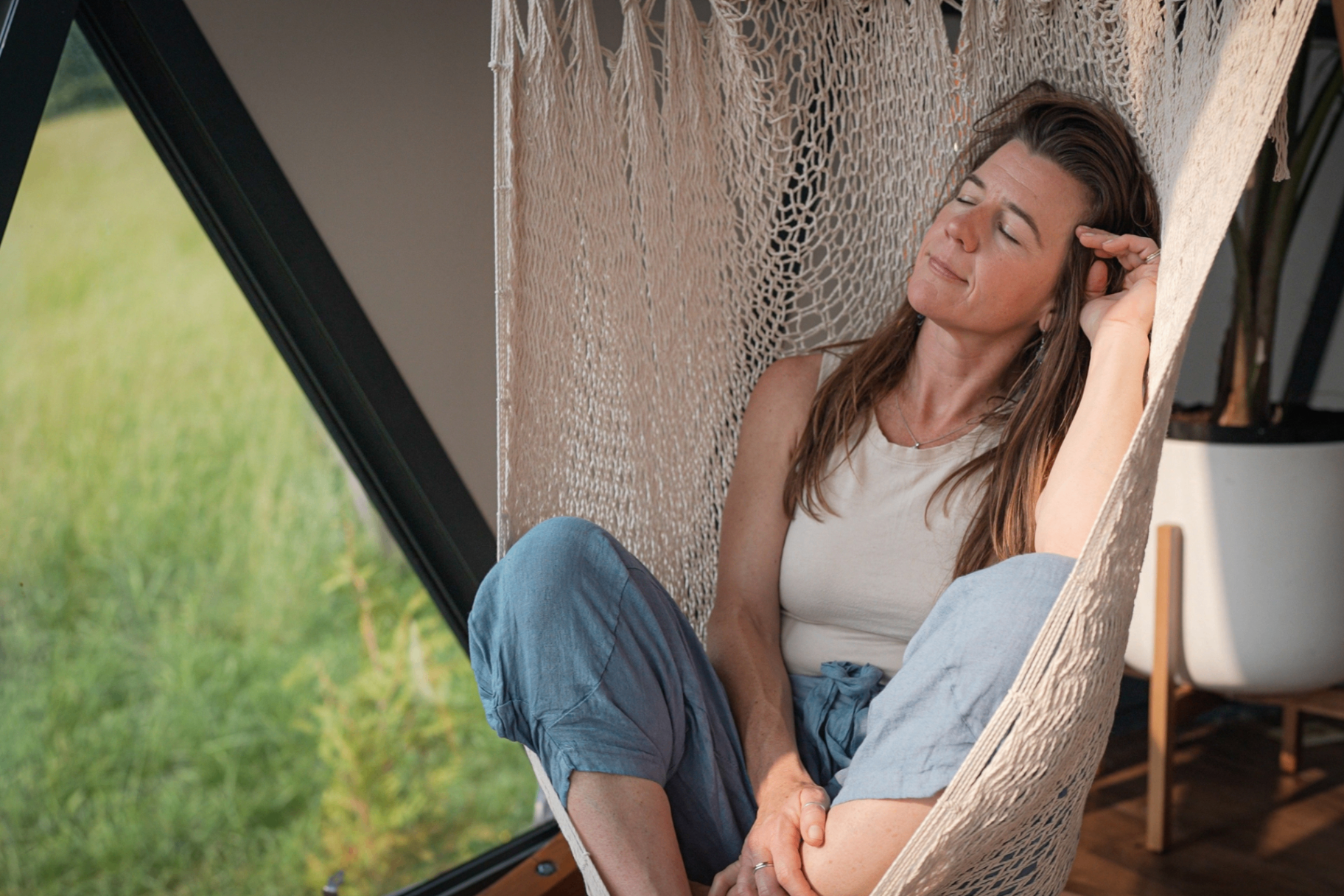 Woman resting in a hammock chair inside a geodesic dome overlooking green hills