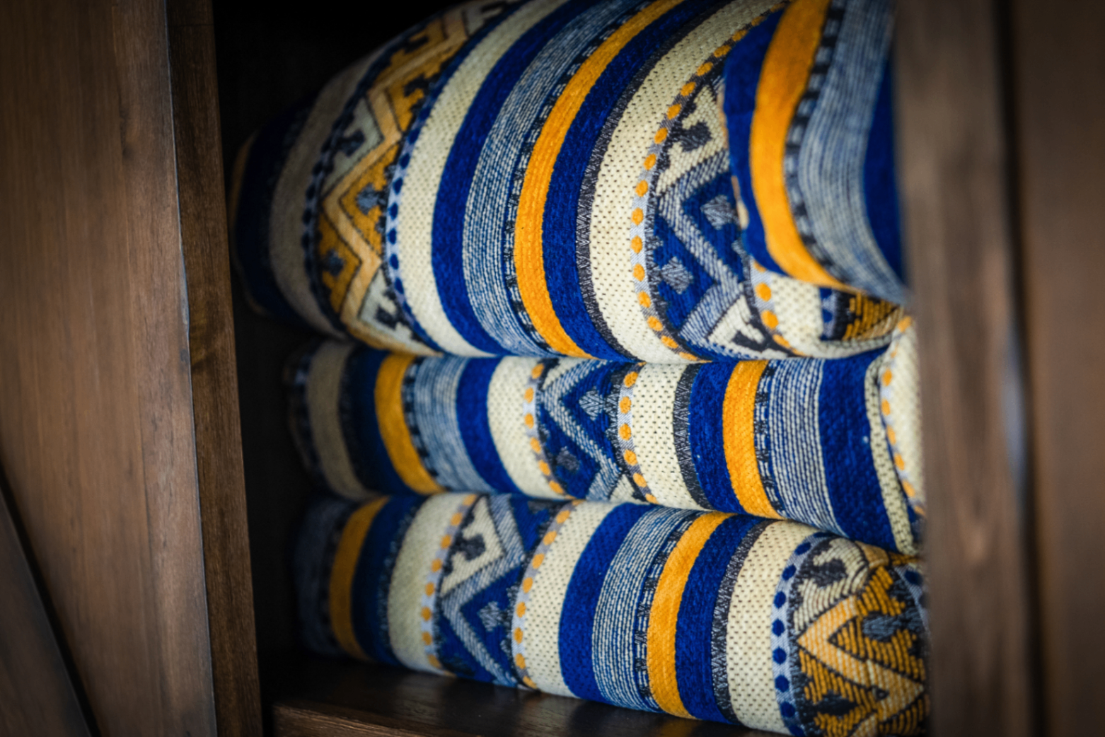 Close-up of folded blue, saffron, and cream kilim blankets stacked on a dark wood shelf
