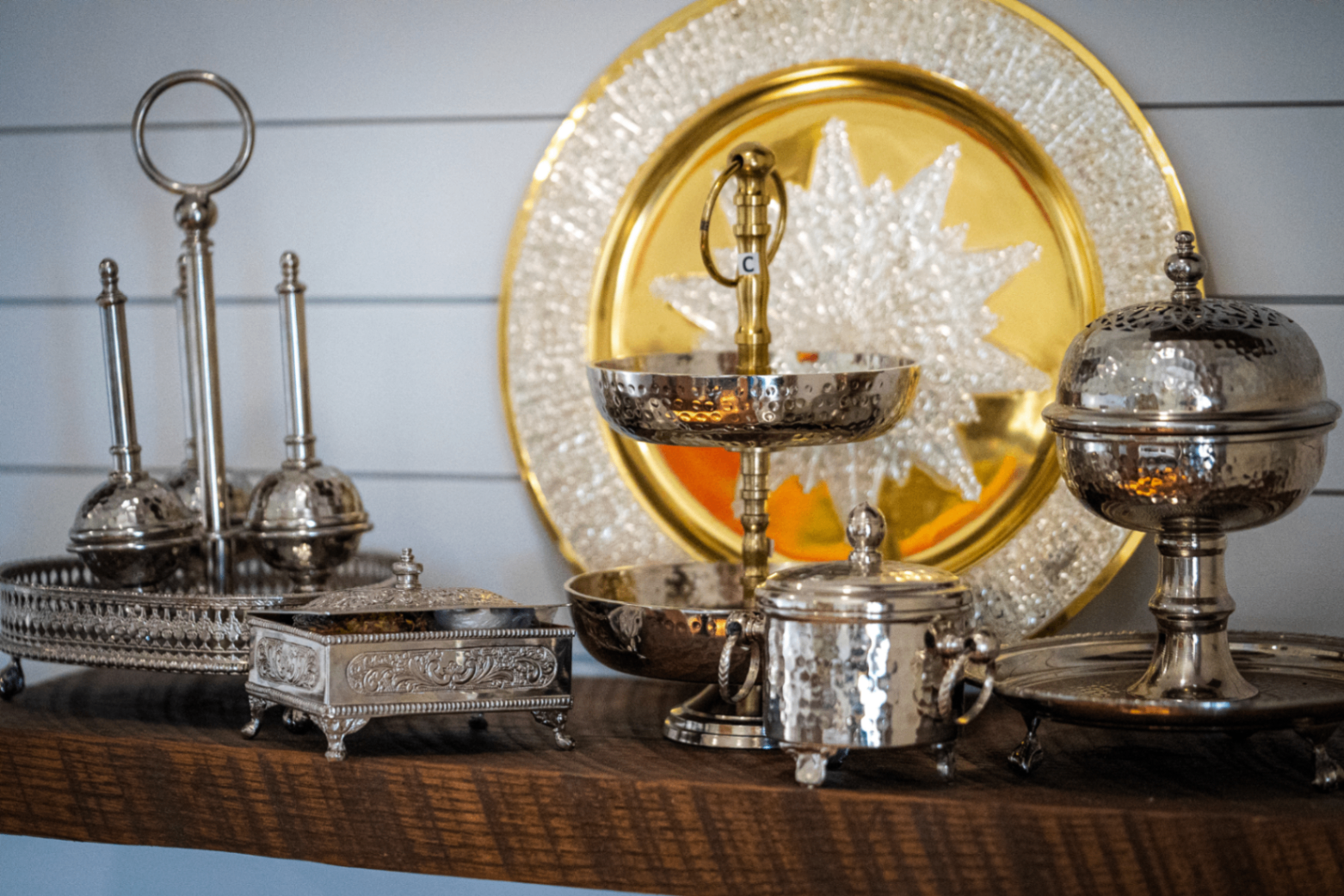 Silver and brass Moroccan tea vessels arranged on a walnut shelf against a golden engraved platter