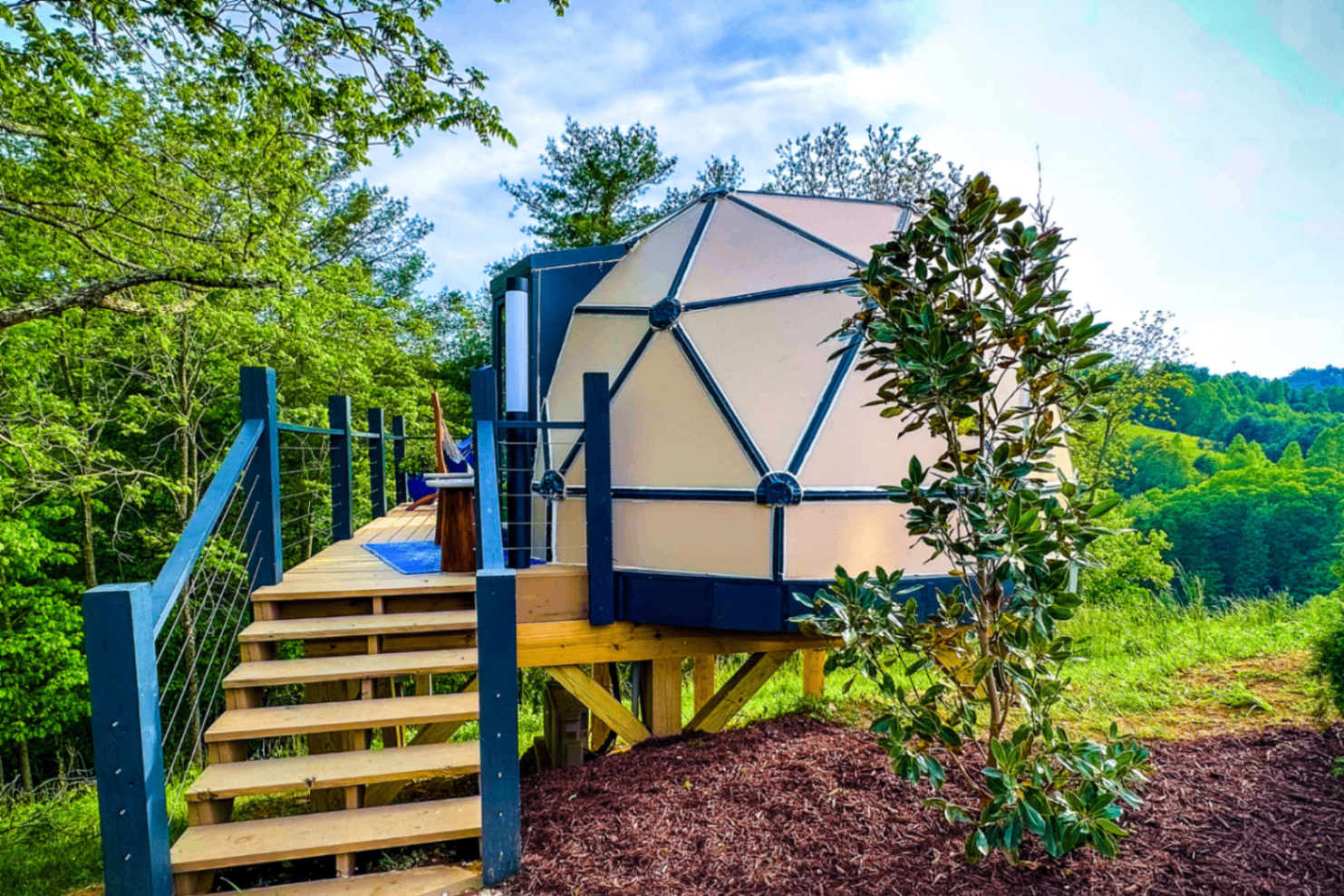 Dome on stilts with a wooden deck, stairs, and hammock overlooking the valley