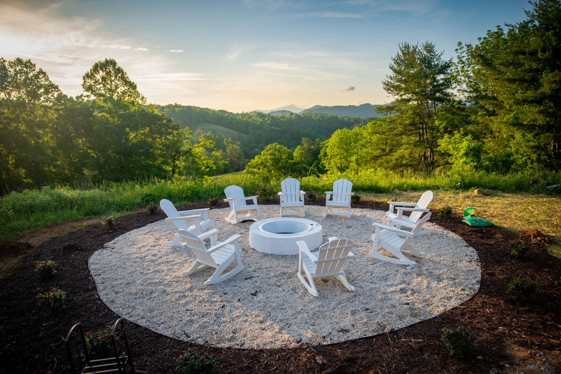 White Adirondack chairs ringing the stone fire pit at sunset with the Blue Ridge beyond