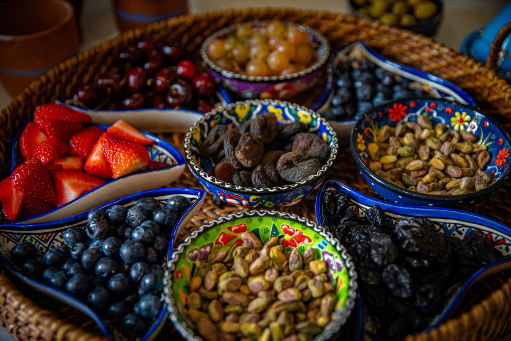 Woven tray of hand-painted Moroccan bowls filled with cherries, strawberries, grapes, blueberries, pistachios, apricots and prunes