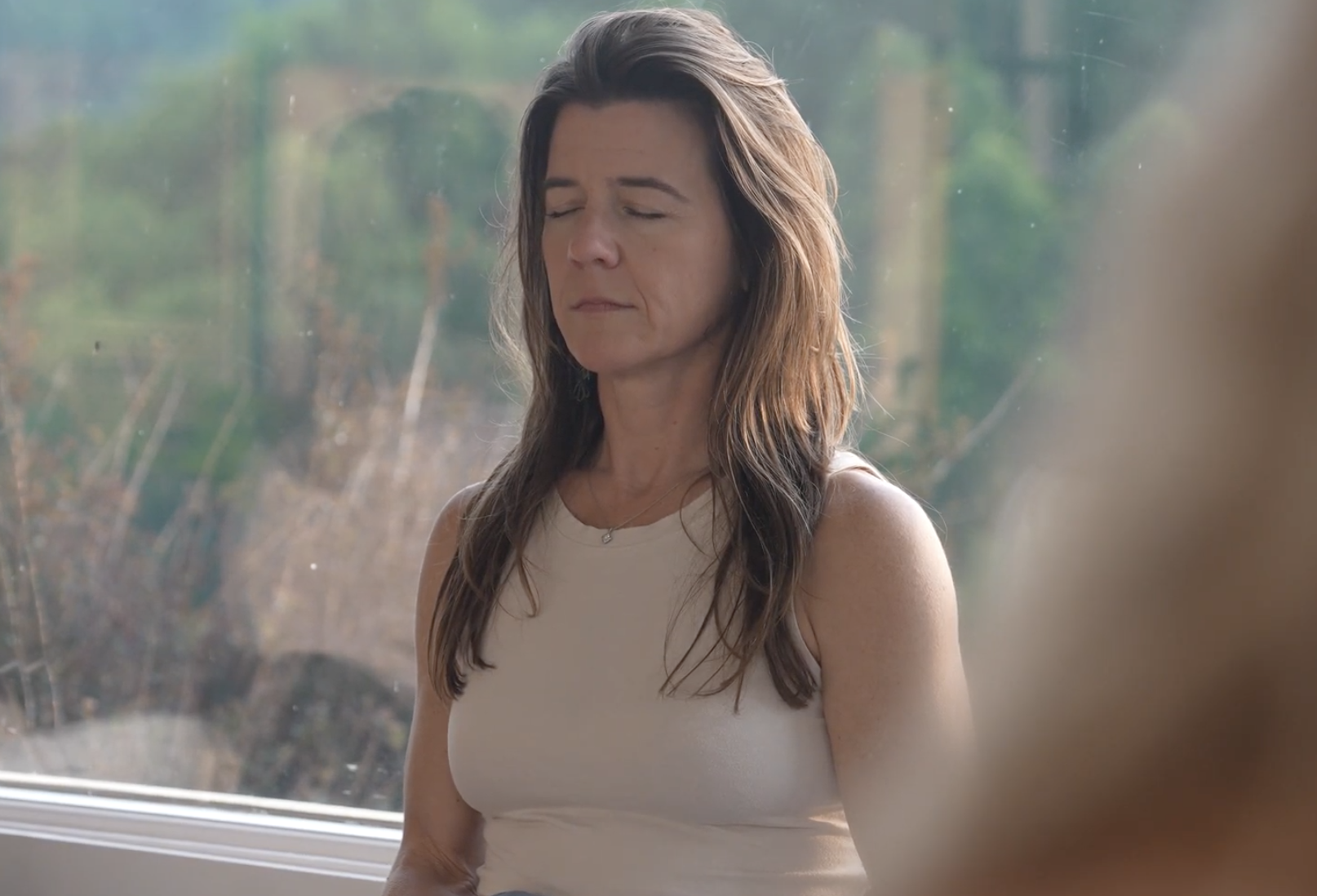 A guest sits in stillness beside a sunlit window, eyes softly closed.