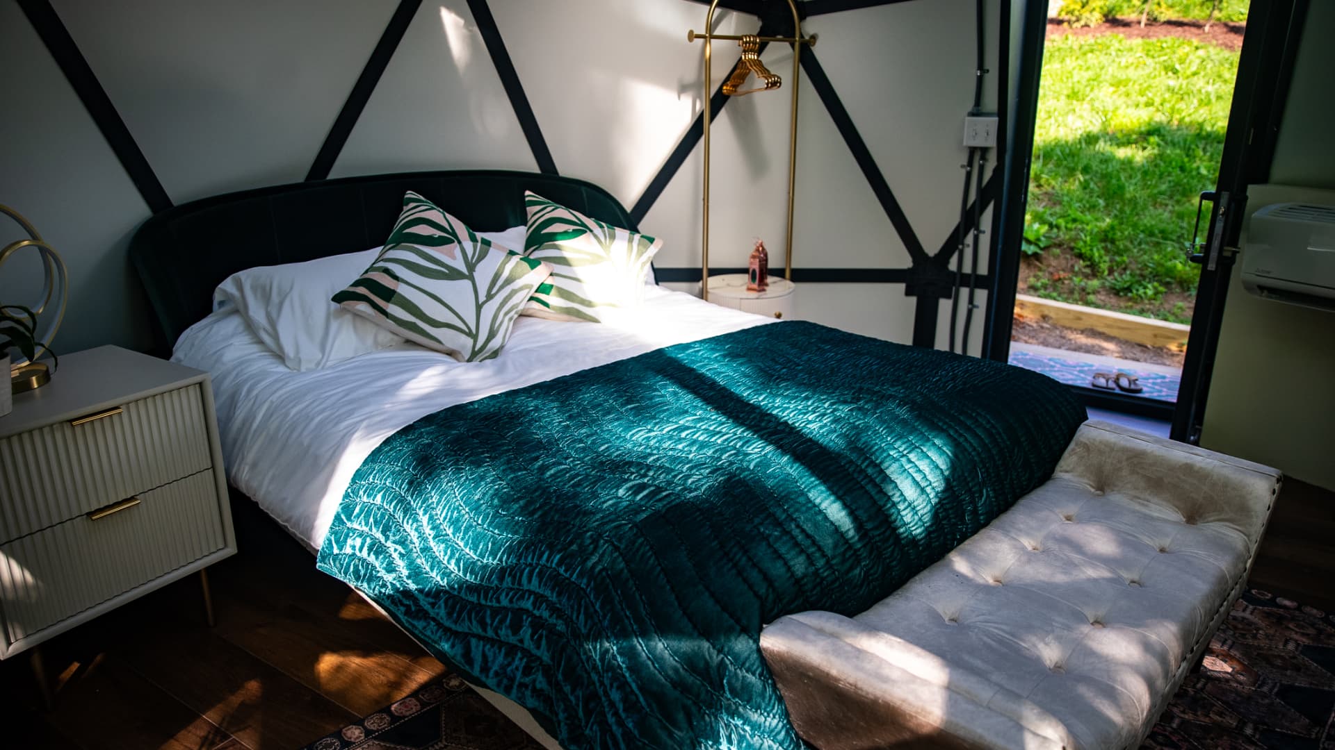 The queen bed in forest green inside the Fes Dome, trees through the glass